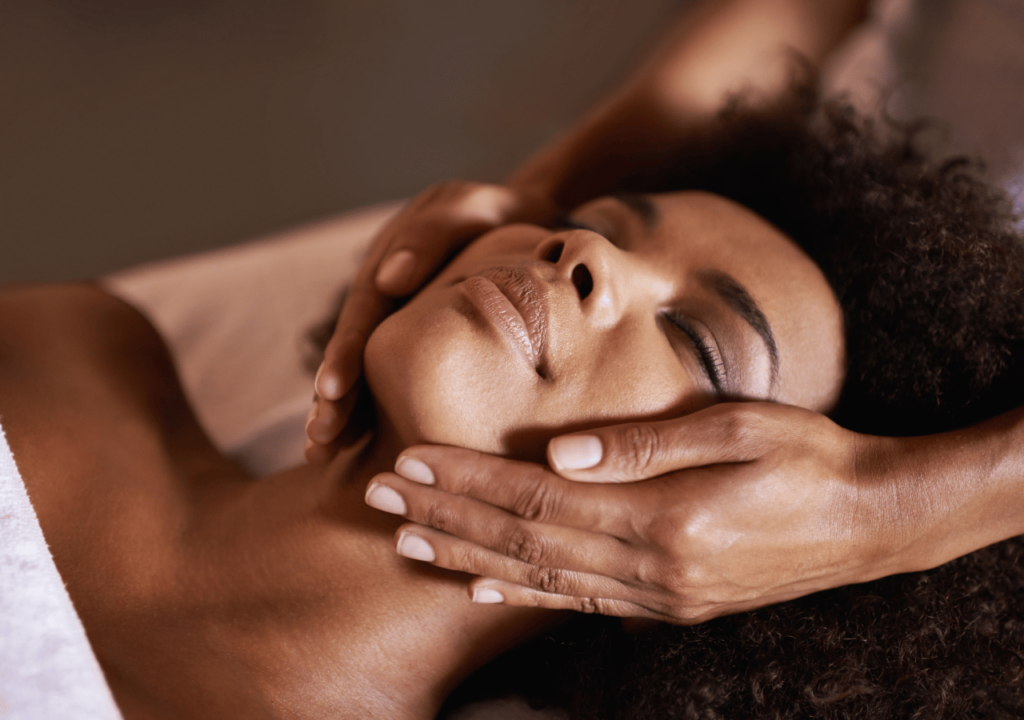 A beautiful woman lying on a bed and another woman is treating her face.