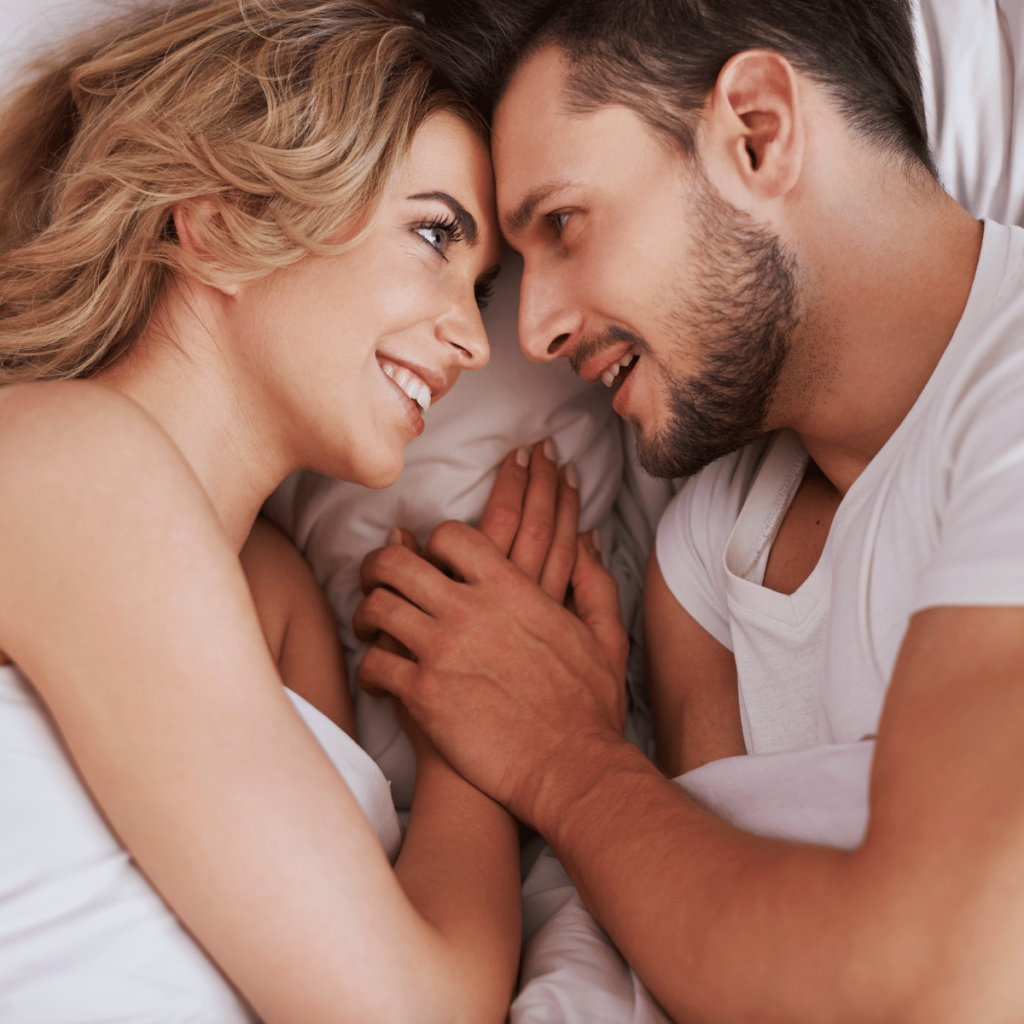 A happy couple holding hands while lying in bed.