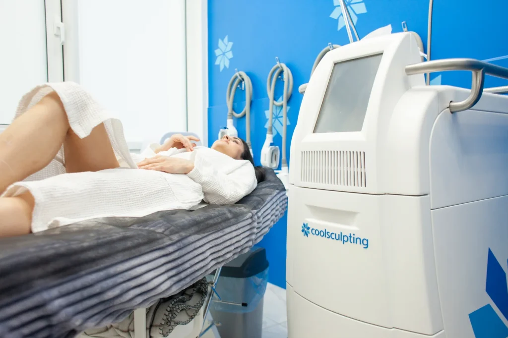 A woman lying in a bed next to a cool sculpting machine getting ready to have a treatment.