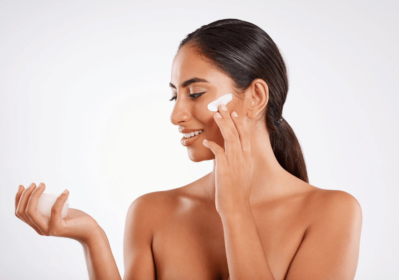 smiling beautiful woman applying cream on her face, with a light grey background